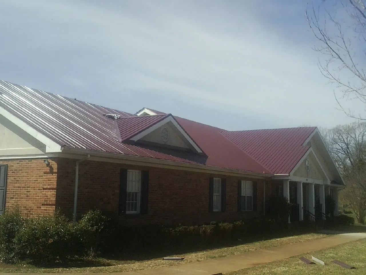 Red metal roof with gabled entries on a long brick building, from a Hail Damage Roof Repair job in Haleyville