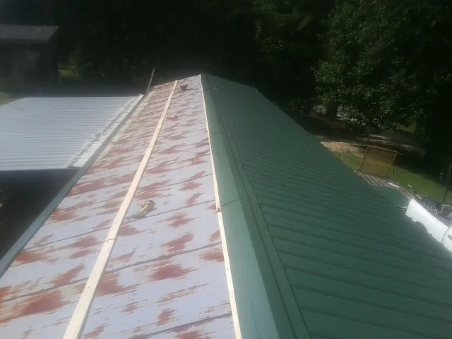 Old rusted panels beside newly installed green metal roofing — Wind Damage Roof Repair by Roofing Brothers in Haleyville