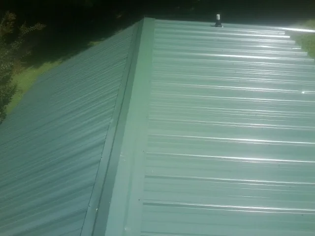 New green metal panels meeting at the ridge of a roof — Flat Roof Repair work by our crew in Haleyville