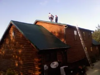 Crew on the ridge of a green metal roof on a two story log home in Haleyville