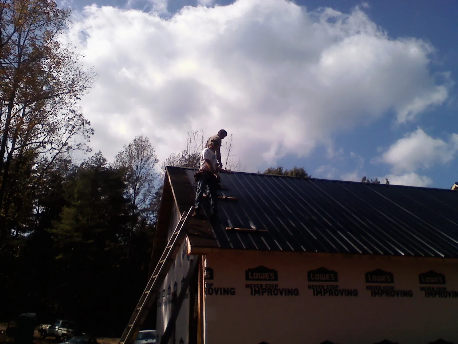 Roofer fastening dark metal panels high against a cloudy sky, from a Roof Inspection job in Haleyville