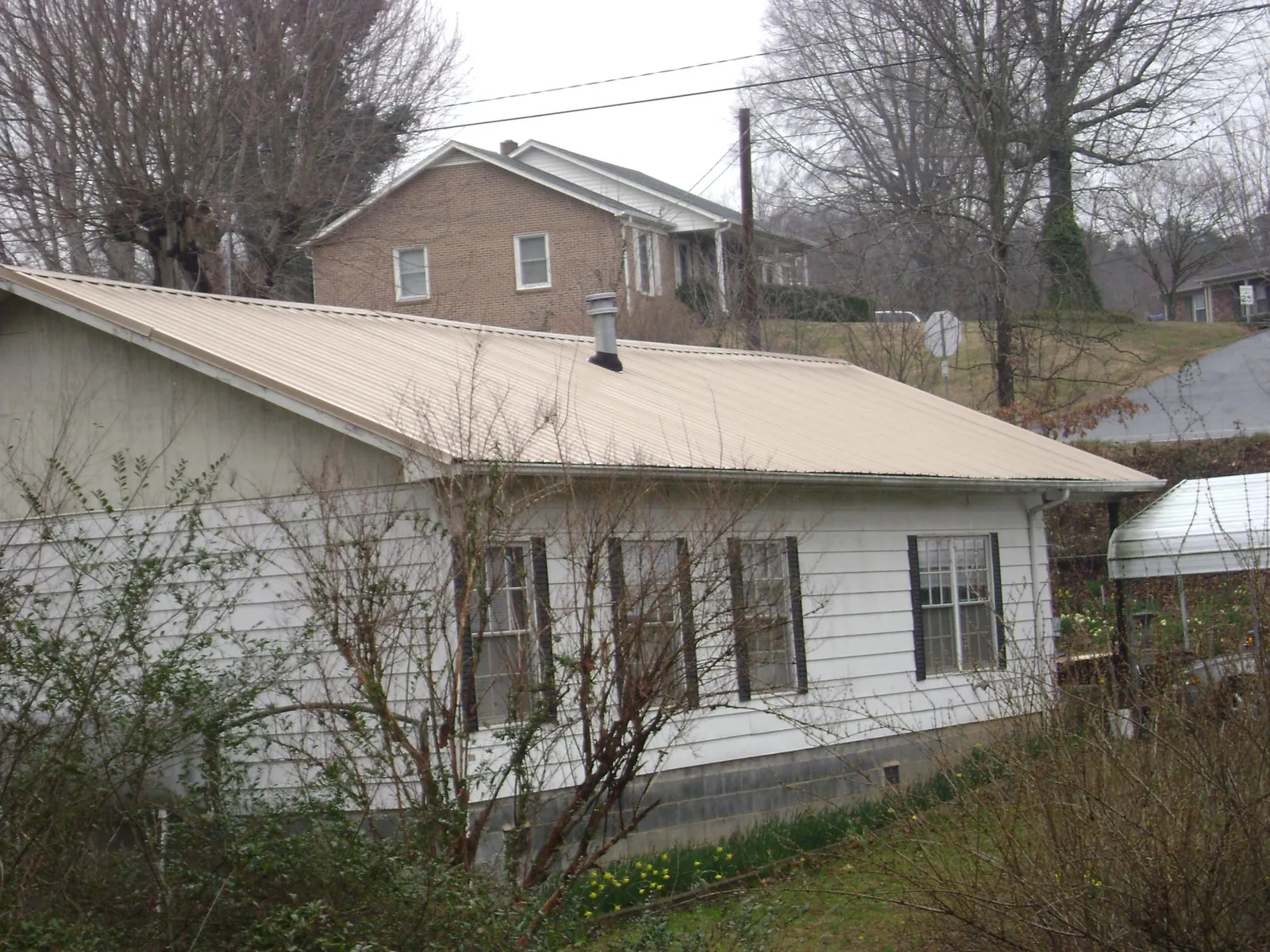Tan metal roof on a white sided house set into a hillside — Commercial Roofing by Roofing Brothers in Haleyville