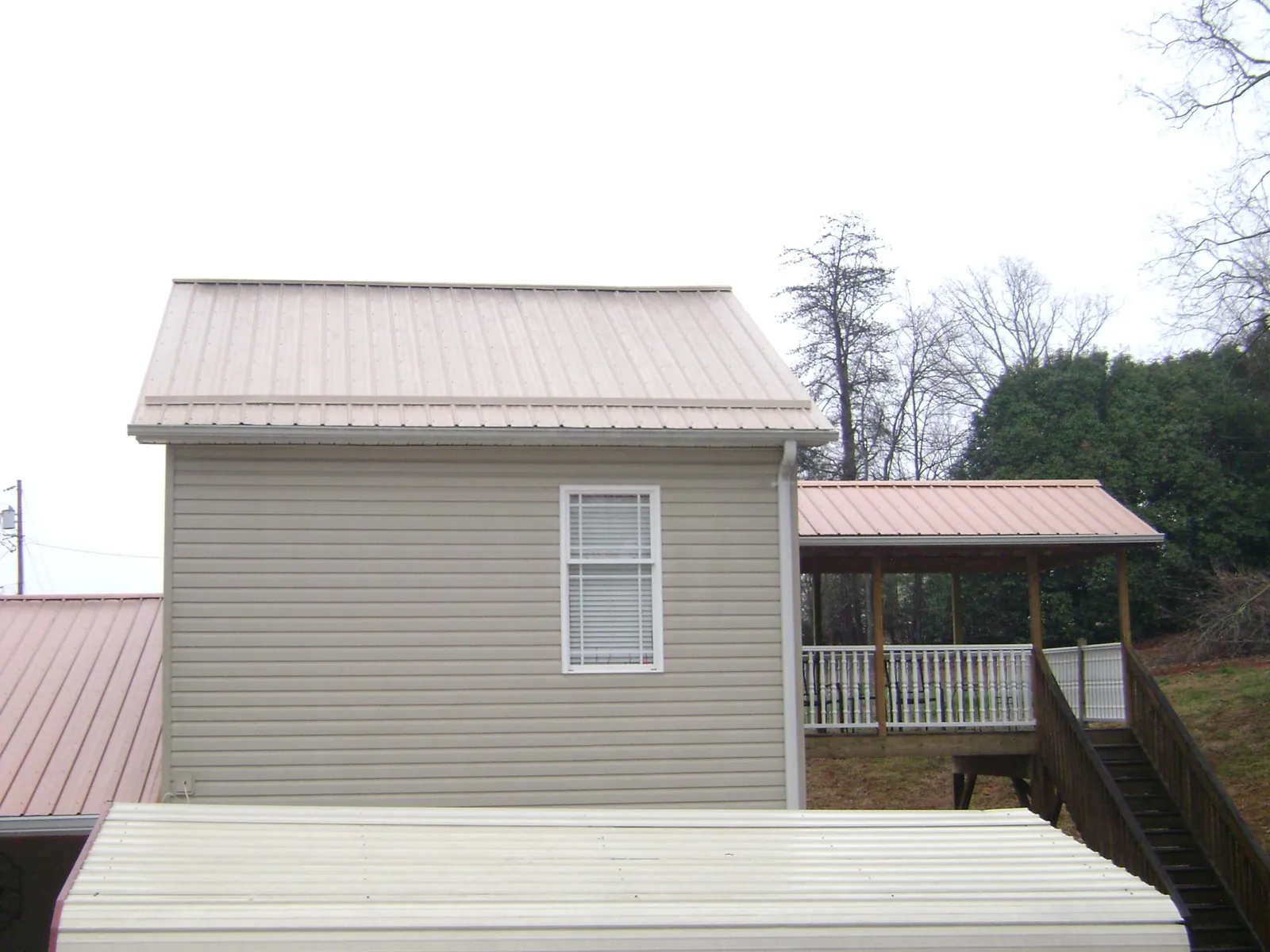 Tan metal roofs on a two story addition and attached porch, from a Roof Replacement job in Haleyville